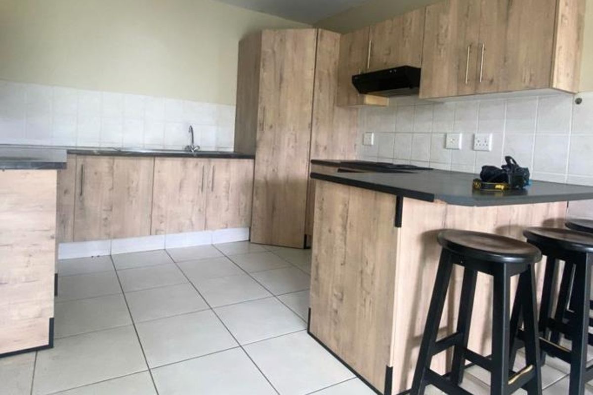A functional kitchen featuring light wood-look cabinetry, dark countertops, a tiled backsplash, and a breakfast bar area with tiled flooring throughout.