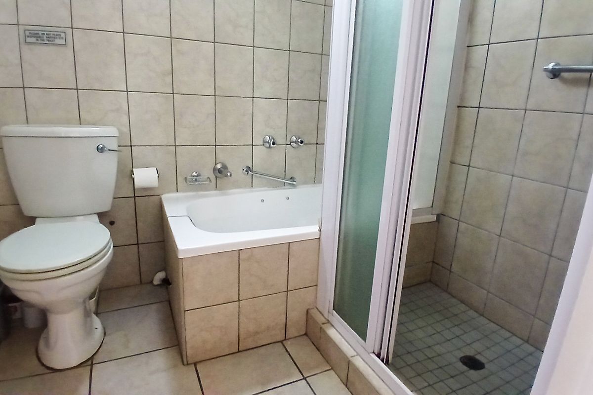 A functional bathroom featuring a bathtub, separate shower enclosure, and tiled finishes throughout, offering a clean and practical layout.