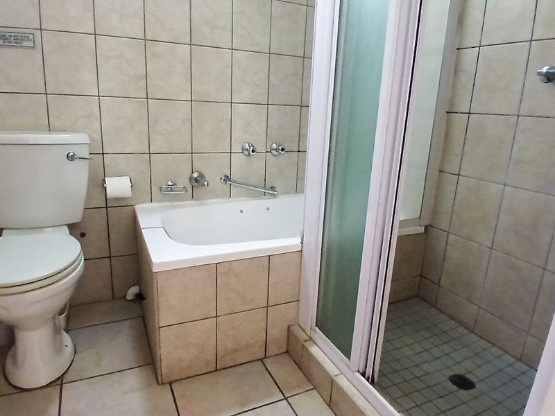 A functional bathroom featuring a bathtub, separate shower enclosure, and tiled finishes throughout, offering a clean and practical layout.