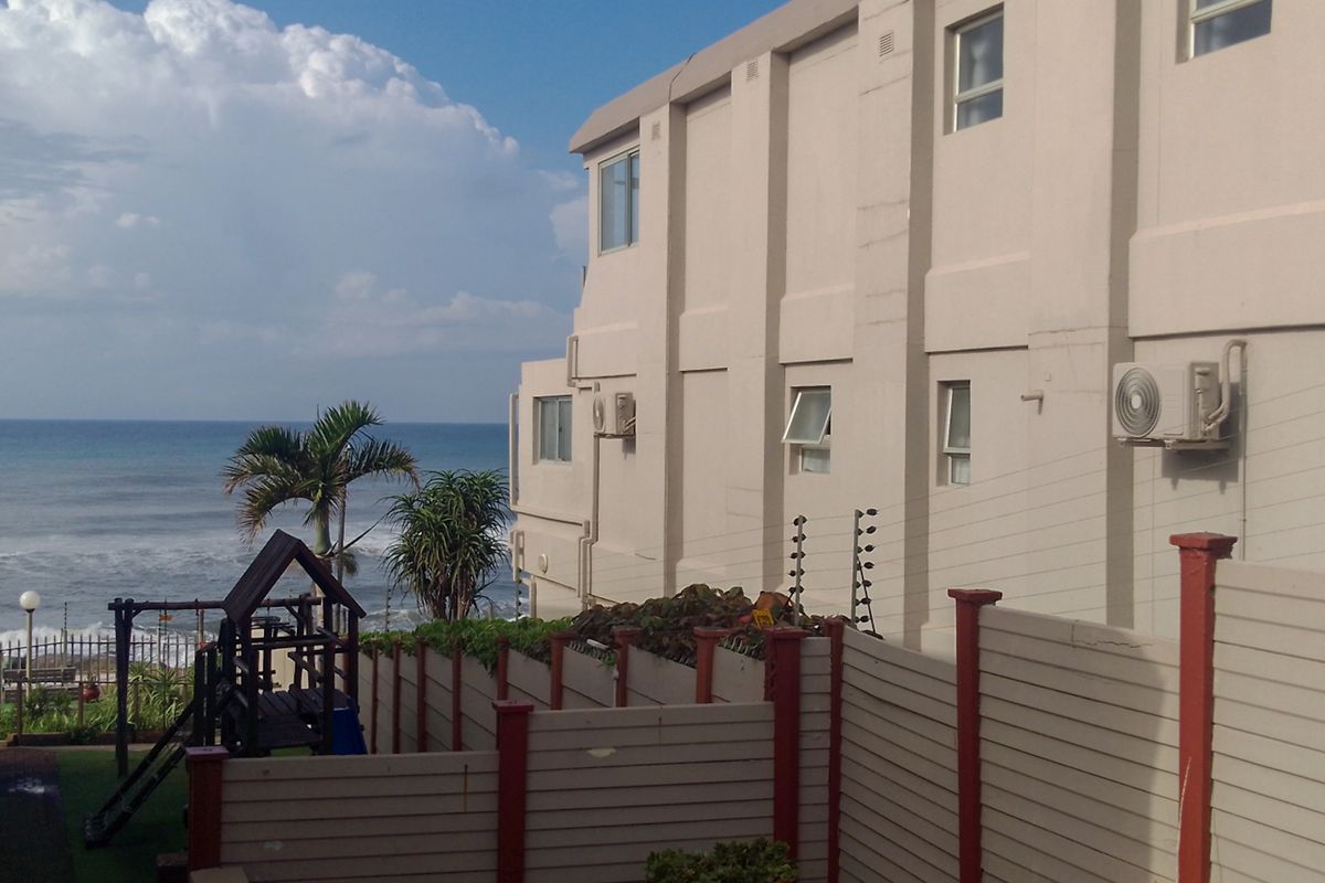 Rear exterior view of the apartment building featuring boundary fencing, electric security, and ocean views.