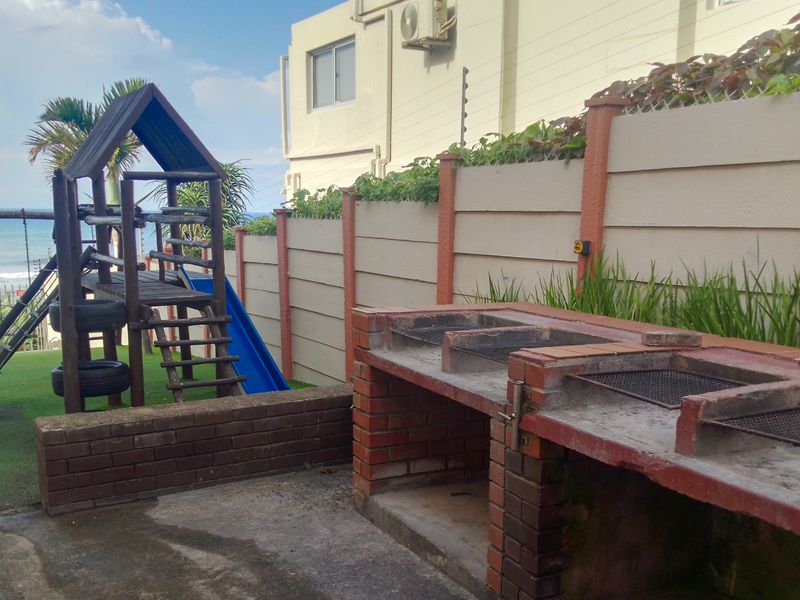 Rear outdoor area featuring a built-in brick braai, paved patio, and artificial lawn, enclosed by a boundary wall with electric fencing.