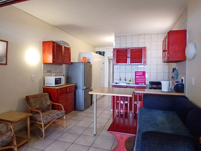 Open-plan living and kitchen area featuring tiled flooring and dated wooden cabinetry, offering a functional layout with potential for modern updates.