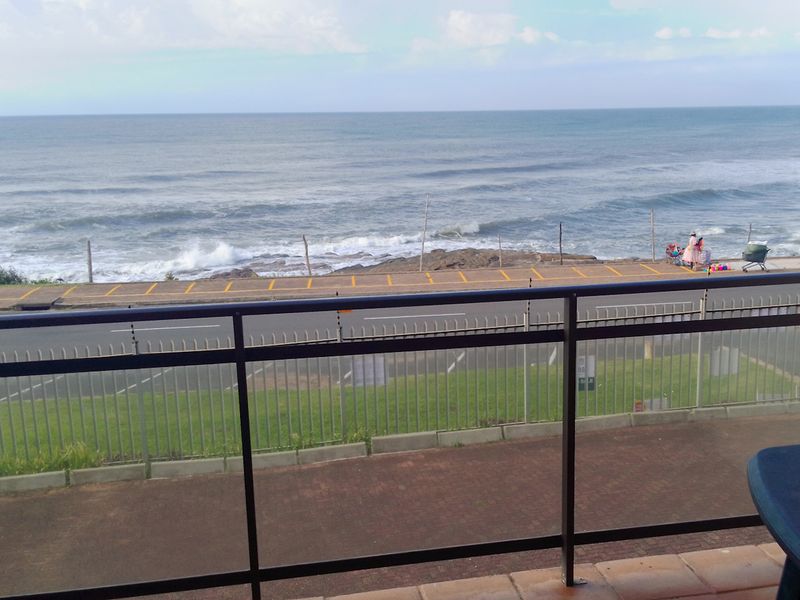 A balcony featuring a metal balustrade and tiled flooring, offering an unobstructed view of the ocean and coastal road.