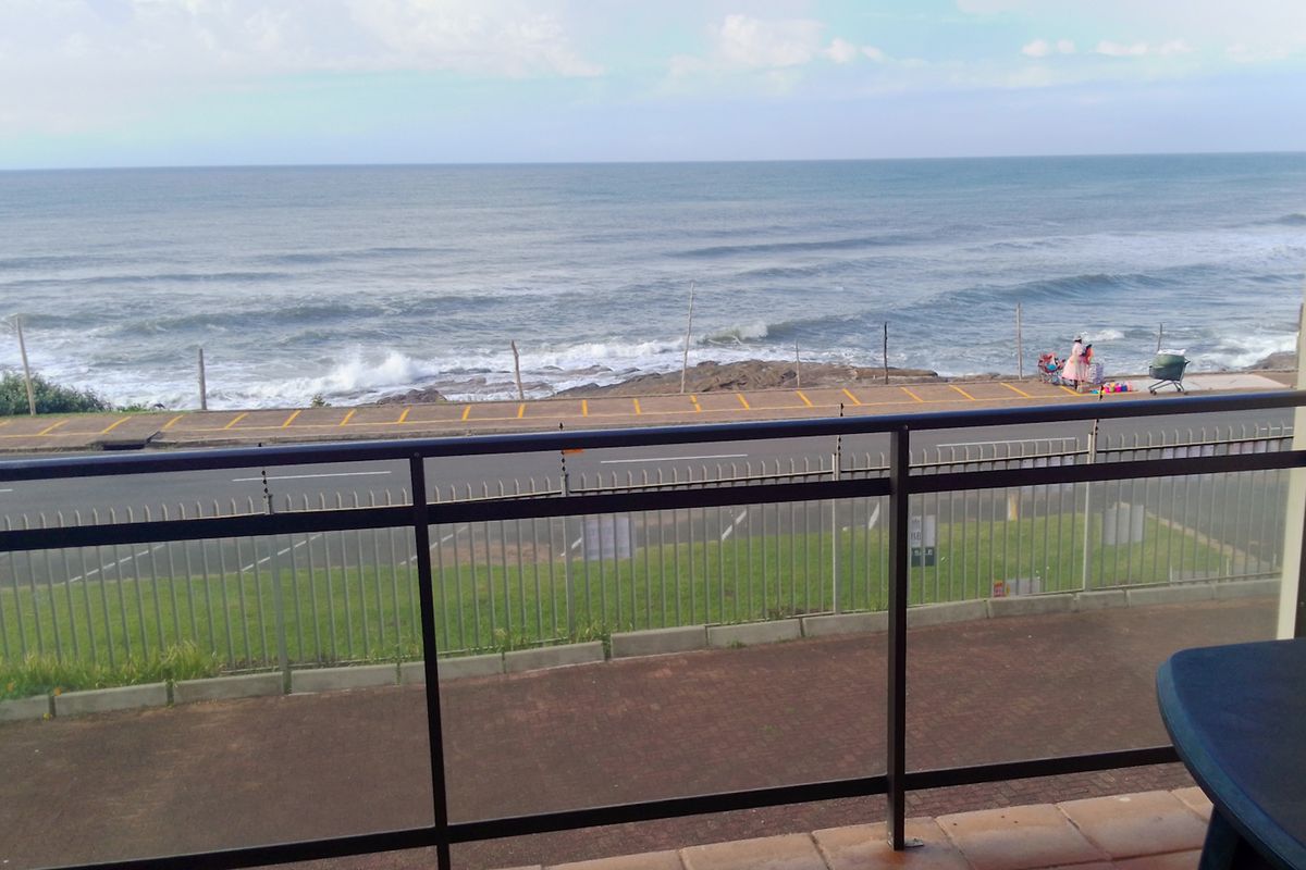 A balcony featuring a metal balustrade and tiled flooring, offering an unobstructed view of the ocean and coastal road.