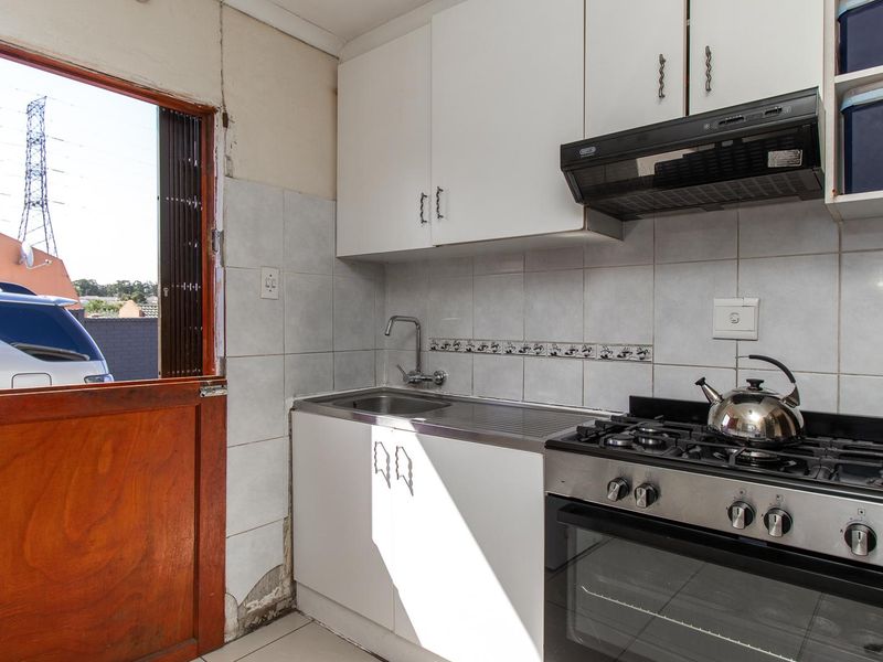 Compact kitchen featuring a gas stove, oven, extractor fan, stainless steel sink, and white cabinetry with tiled splashbacks and direct outdoor access.