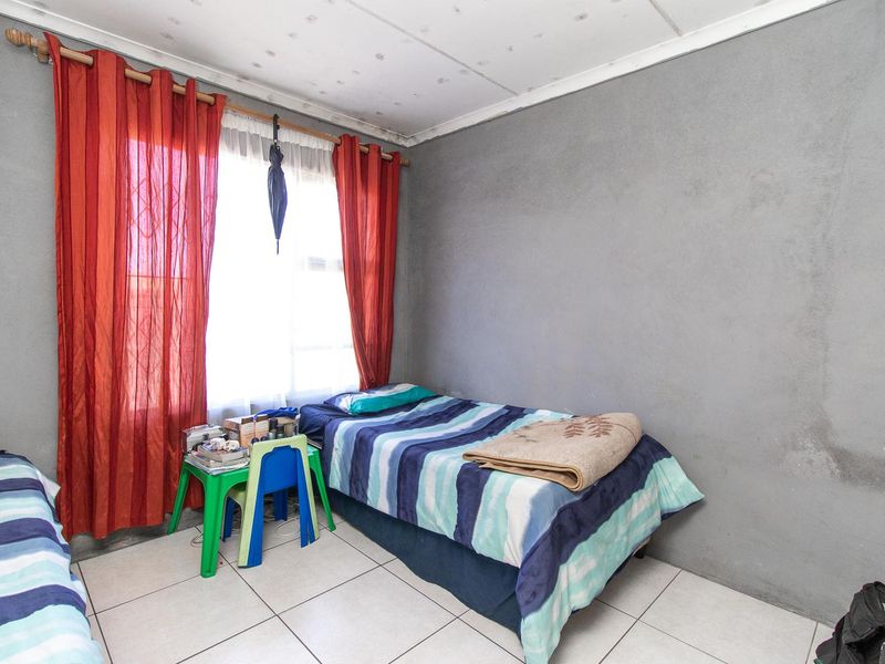 A bedroom featuring tiled flooring and a ceiling tile finish, currently showing signs of wear and wall staining.