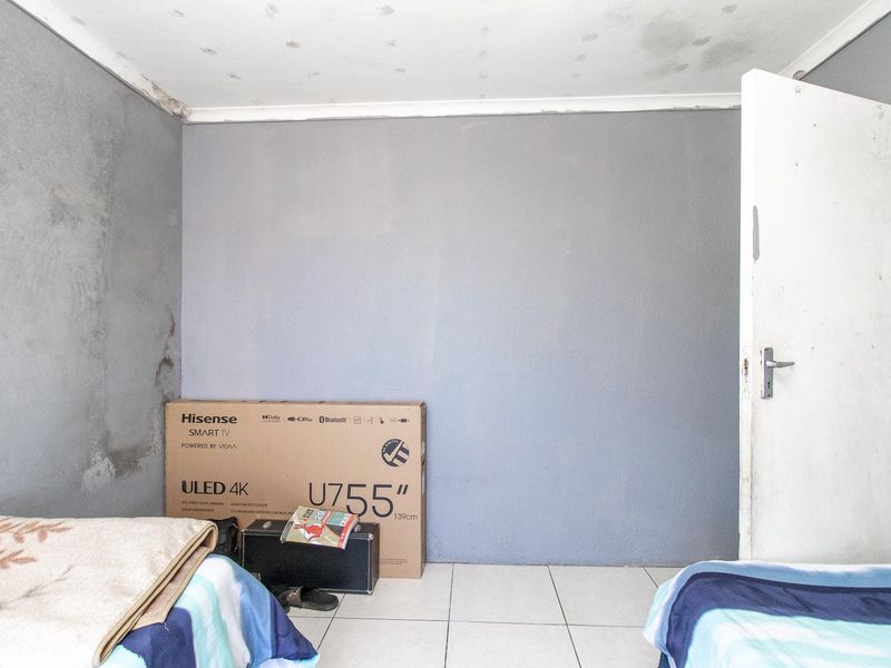 A bedroom featuring tiled flooring and visible signs of wall dampness and ceiling water damage, requiring maintenance and cosmetic repair.