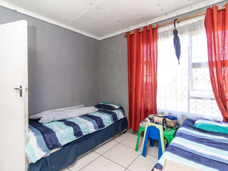 A bedroom featuring tiled flooring and a security gate on the window, showing signs of ceiling water damage and paint wear.