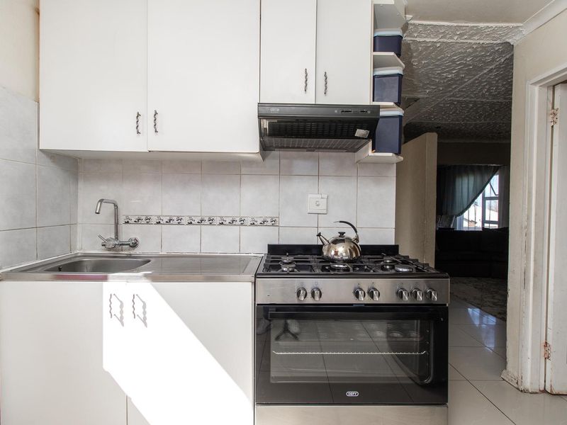 Compact kitchen featuring white cabinetry, tiled backsplash, stainless steel sink, and a built-in gas stove with oven.