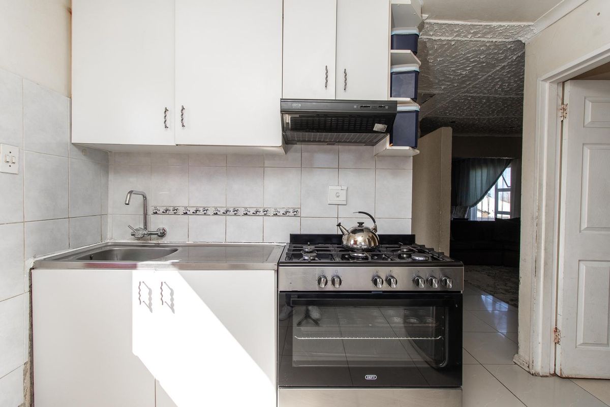 Compact kitchen featuring white cabinetry, tiled backsplash, stainless steel sink, and a built-in gas stove with oven.