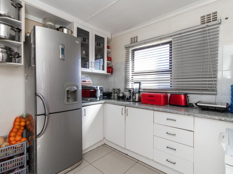 A functional kitchen featuring white built-in cabinetry, laminate countertops, tiled splashbacks, and tiled flooring with natural light from a window.