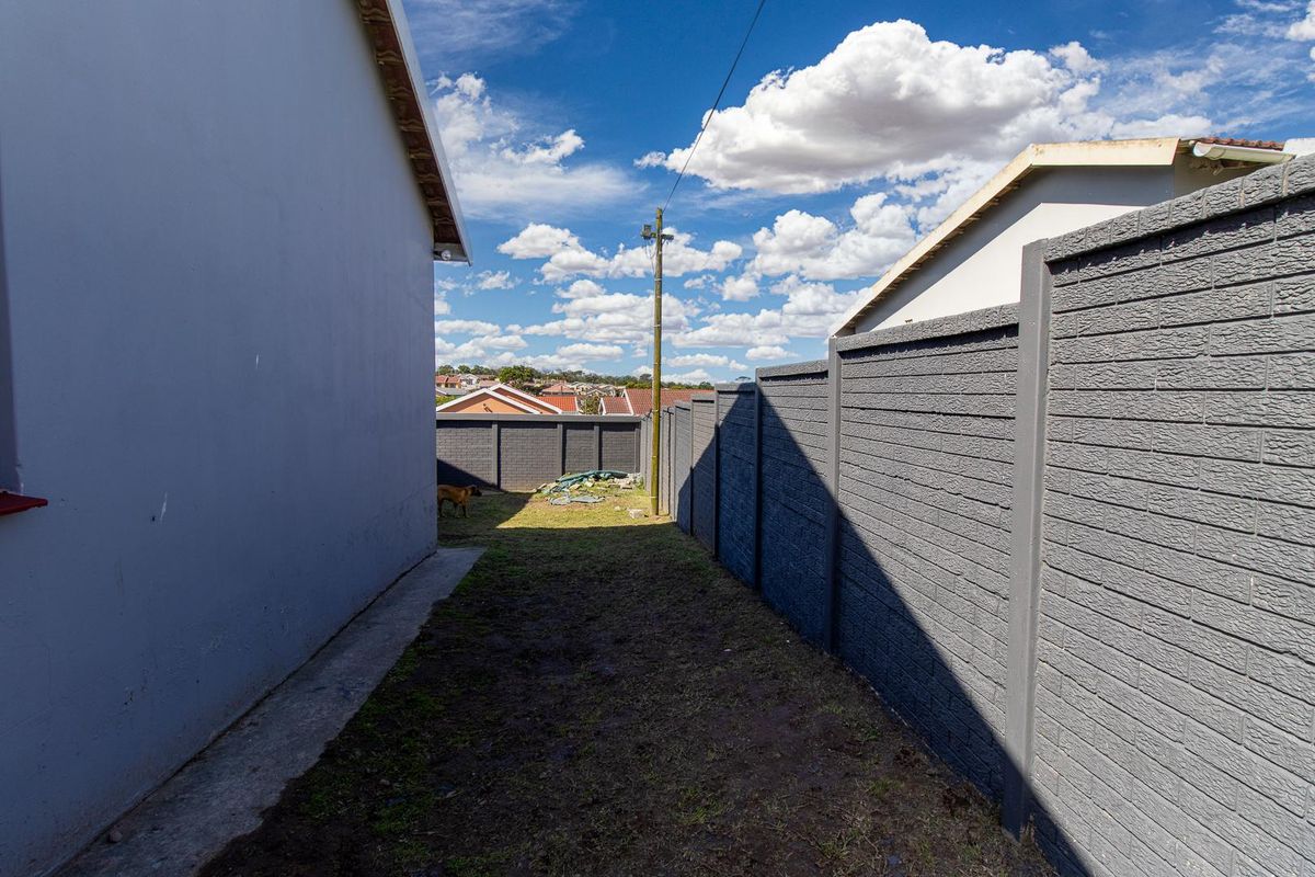 A side yard area featuring a precast concrete boundary wall and a concrete pathway along the side of the house.