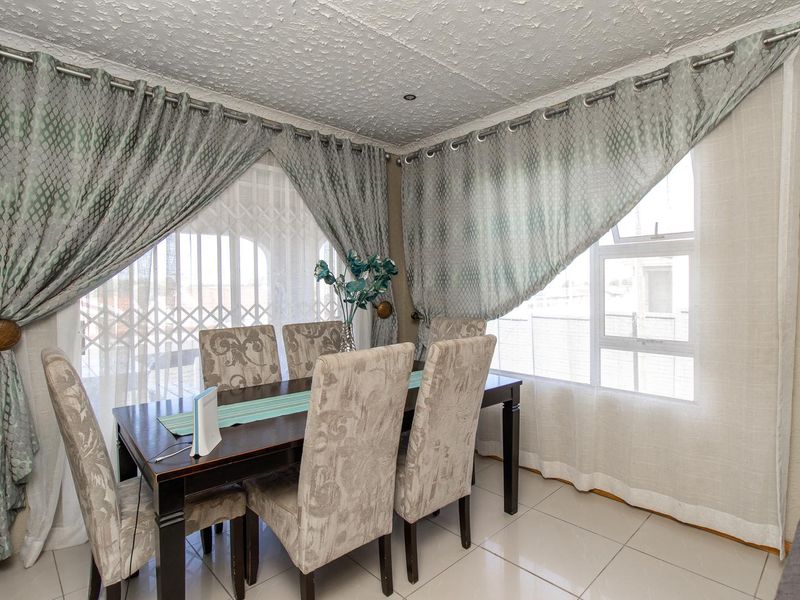 A dining room featuring tiled flooring, textured ceilings with recessed lighting, and large windows with curtain treatments.