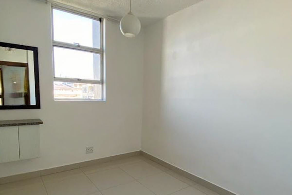 A bright, empty bedroom featuring tiled flooring, a built-in vanity unit, and a large window providing natural light.