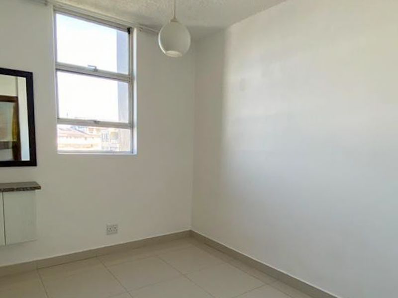 A bright, empty bedroom featuring tiled flooring, a built-in vanity unit, and a large window providing natural light.