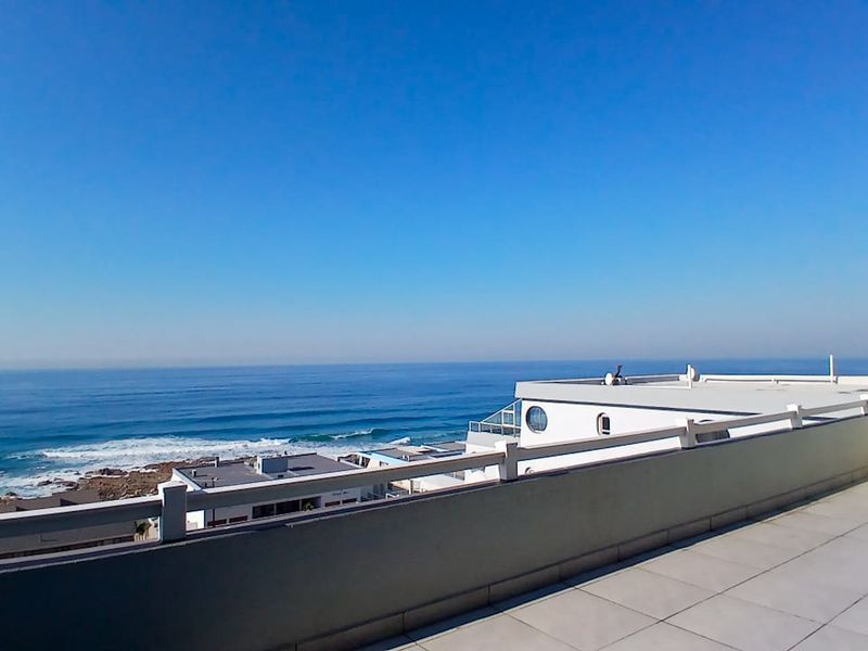 Spacious balcony featuring tiled flooring and a protective railing, offering expansive, unobstructed views of the ocean and coastline.
