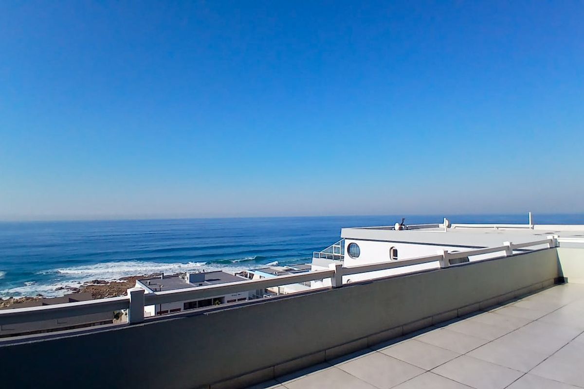 Spacious balcony featuring tiled flooring and a protective railing, offering expansive, unobstructed views of the ocean and coastline.