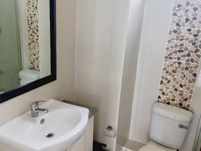 A clean, functional bathroom featuring a vanity with a ceramic basin, a toilet, and a shower enclosure with decorative stone mosaic wall accents.