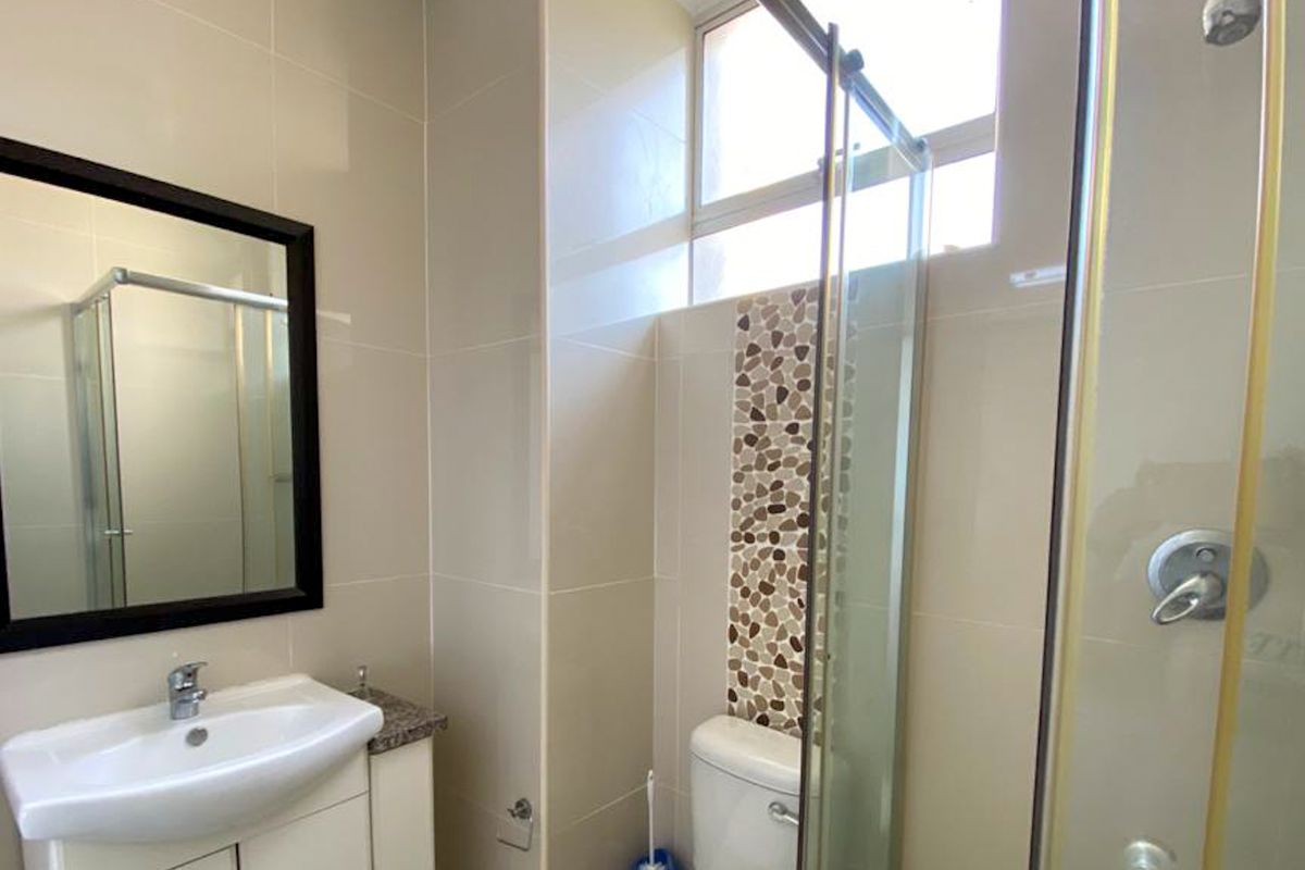 A modern bathroom featuring a vanity cabinet with a ceramic basin, a glass shower enclosure, and decorative pebble mosaic accent tiling.