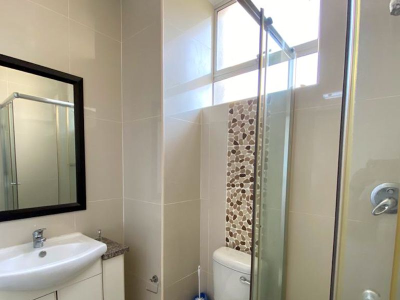 A modern bathroom featuring a vanity cabinet with a ceramic basin, a glass shower enclosure, and decorative pebble mosaic accent tiling.