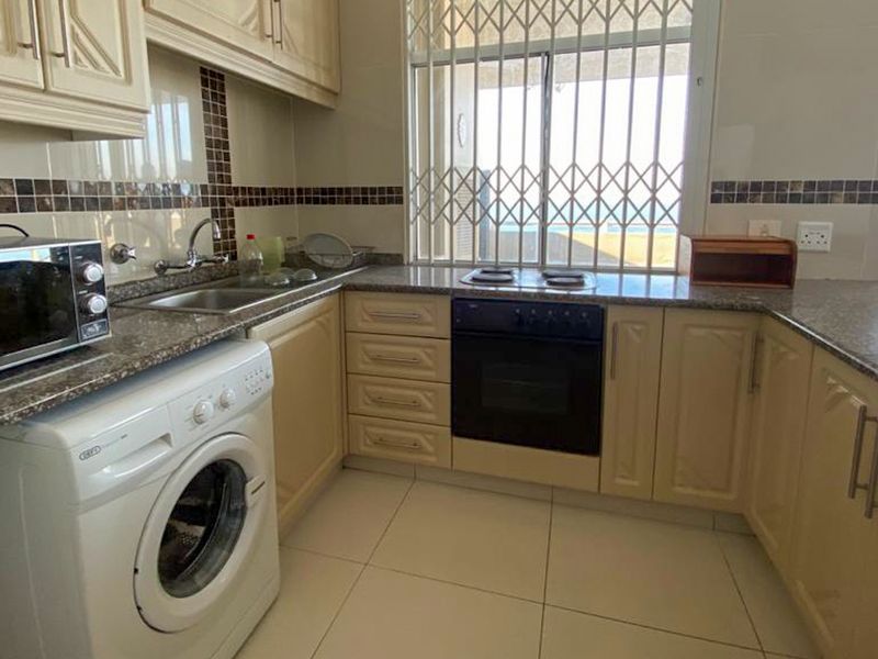 A functional kitchen featuring granite countertops, built-in oven, electric hob, and tiled finishes, with a window overlooking the exterior.