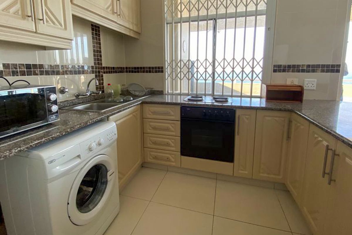 A functional kitchen featuring granite countertops, built-in oven, electric hob, and tiled finishes, with a window overlooking the exterior.