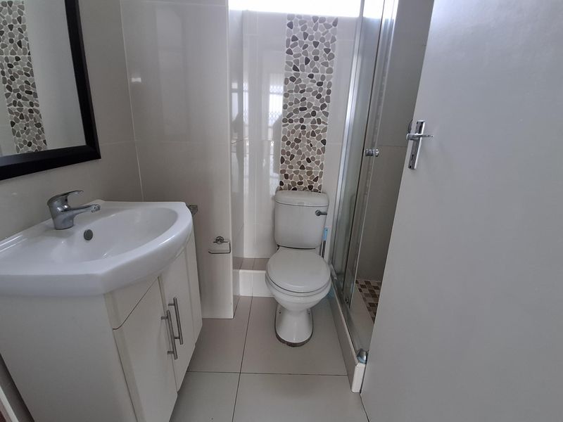 A compact, modern bathroom featuring a vanity cabinet with basin, a standard toilet, and a glass-enclosed shower with decorative pebble tile accents.