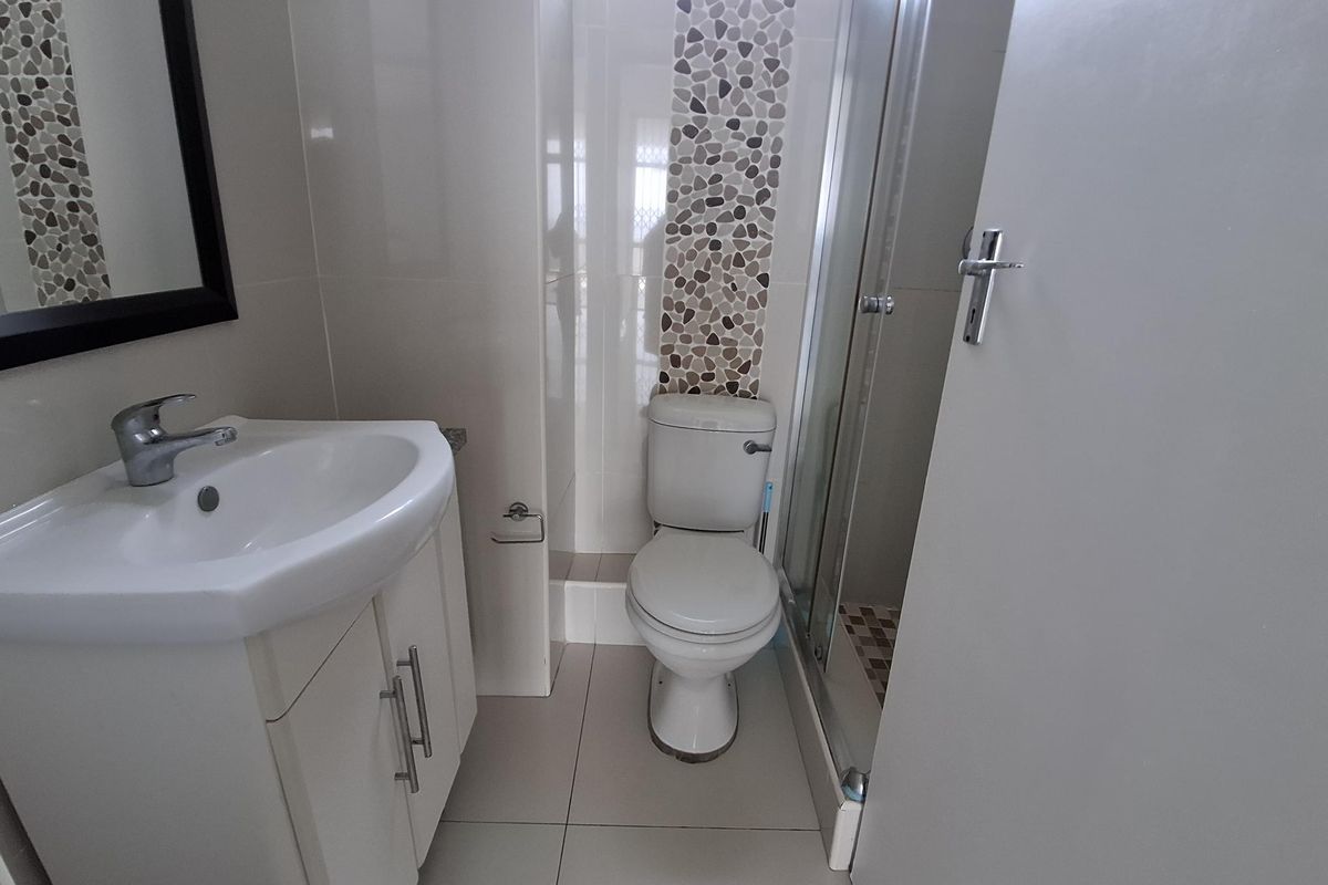 A compact, modern bathroom featuring a vanity cabinet with basin, a standard toilet, and a glass-enclosed shower with decorative pebble tile accents.
