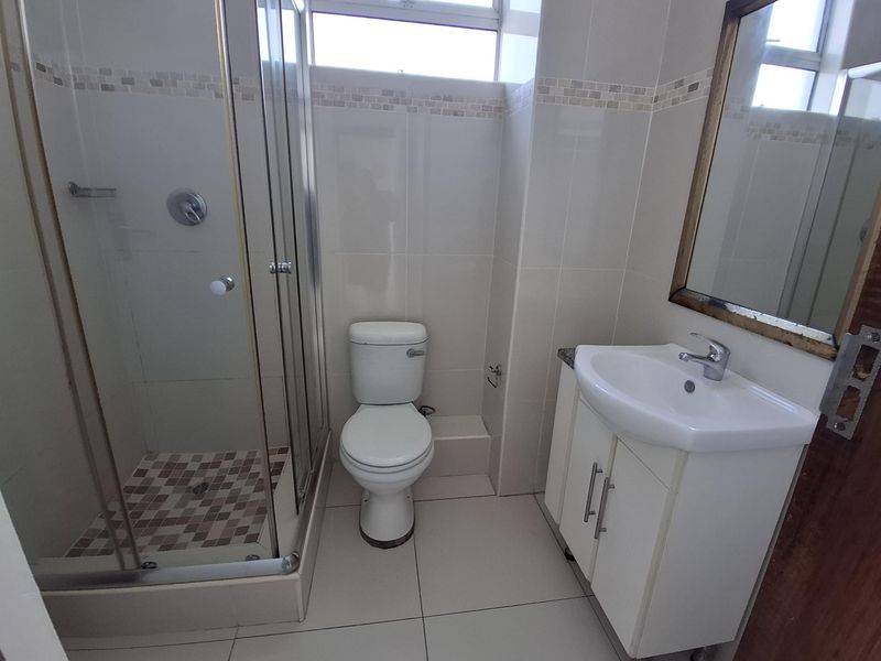 A functional bathroom featuring a glass shower enclosure, a white vanity cabinet with a basin, and neutral wall and floor tiling.