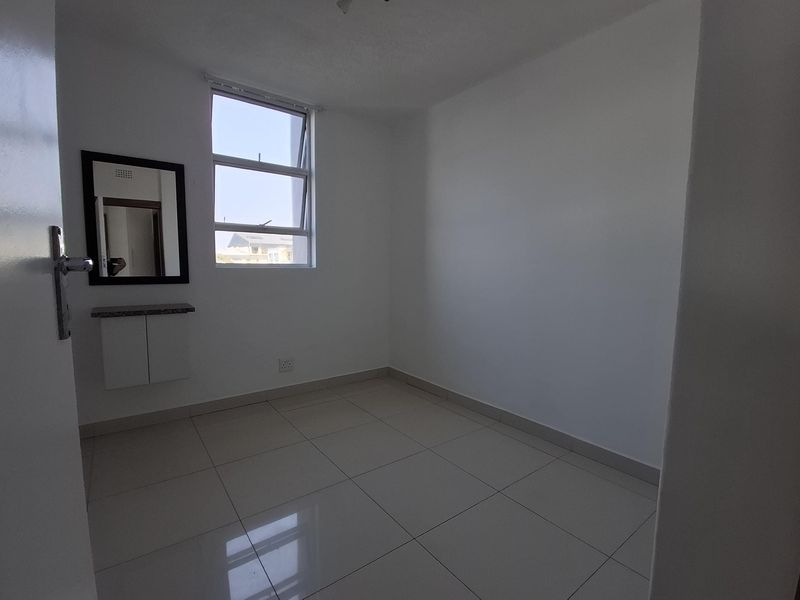 A clean, empty bedroom featuring neutral tiled flooring, a built-in vanity unit, and a large window providing natural light.