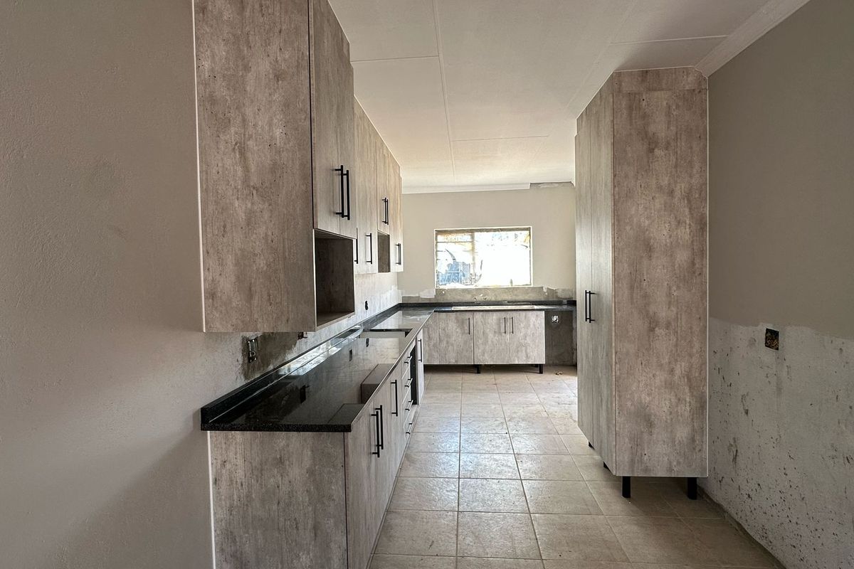 A spacious kitchen featuring modern laminate cabinetry, granite countertops, and tiled flooring, currently undergoing final finishing touches and awaiting appliance installation.
