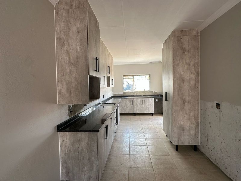 A spacious kitchen featuring modern laminate cabinetry, granite countertops, and tiled flooring, currently undergoing final finishing touches and awaiting appliance installation.