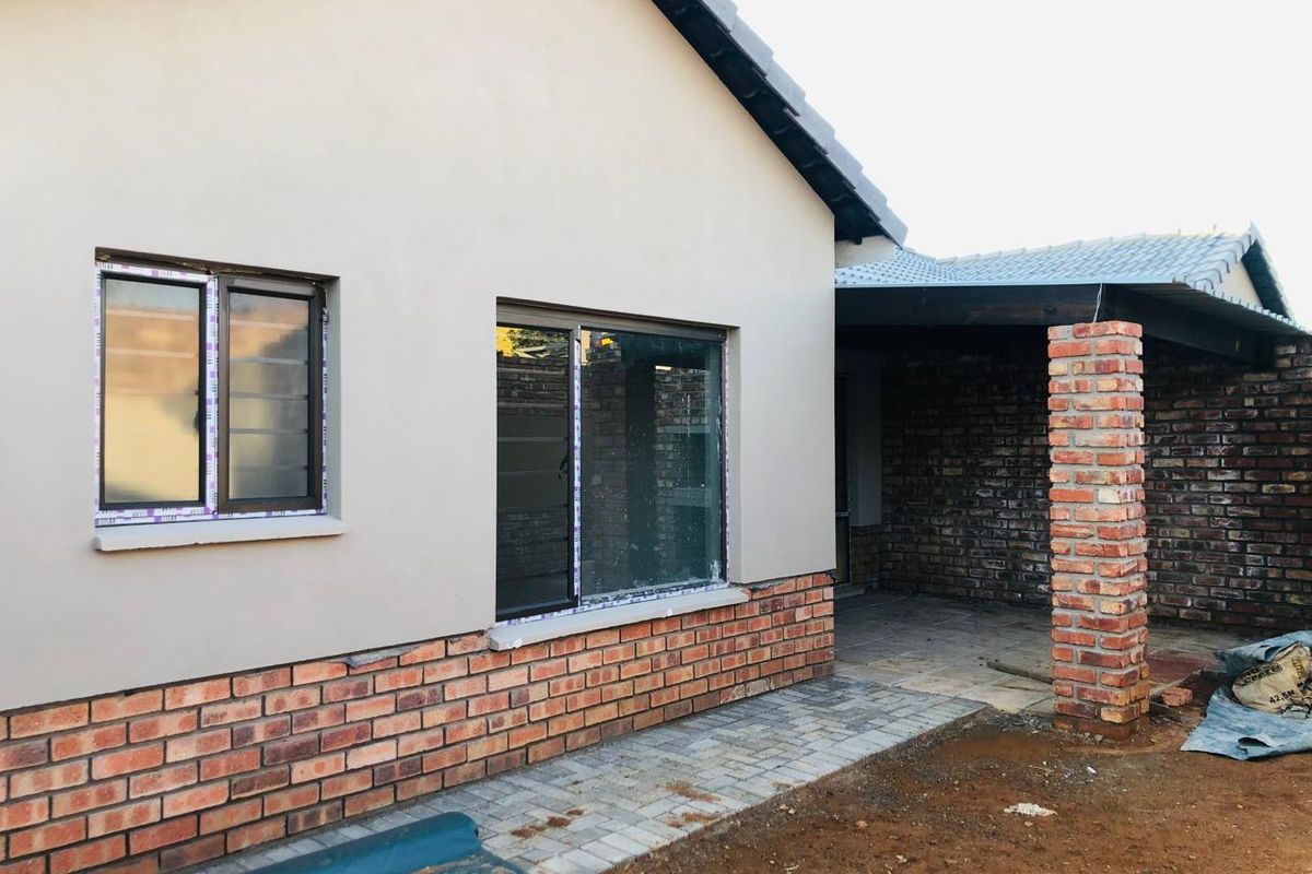 Rear exterior view of a townhouse featuring a combination of plastered and face-brick walls, a paved patio area, and a covered walkway.