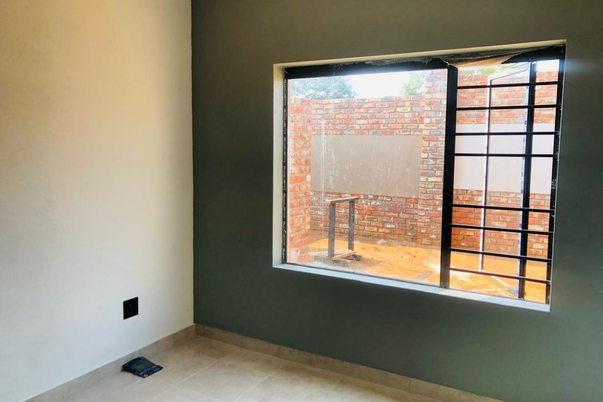 An empty bedroom featuring tiled flooring and a large window with security bars, currently undergoing finishing touches.