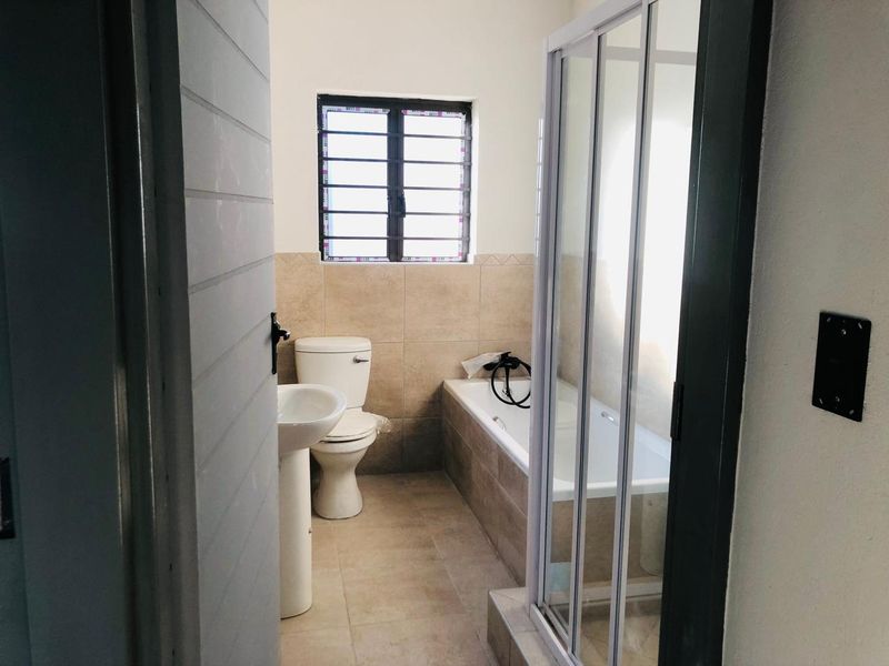 A clean, functional bathroom featuring a pedestal basin, toilet, bathtub, and a separate shower enclosure with neutral wall and floor tiling.