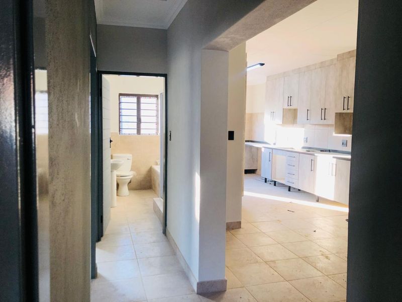 A view from the hallway looking into an empty kitchen and a bathroom, featuring tiled floors and built-in cabinetry.