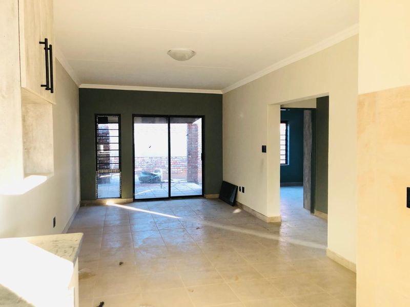 An empty open-plan living area featuring tiled floors, neutral wall tones, and a sliding glass door providing access to the rear patio.