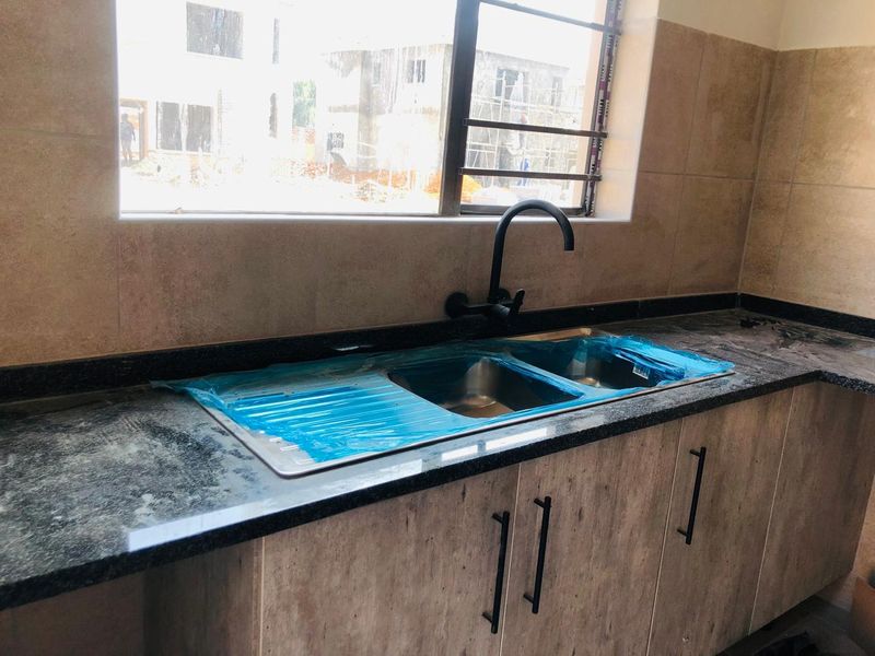 A modern kitchen area featuring a granite countertop, stainless steel double sink with a matte black faucet, and contemporary cabinetry with tiled backsplash.