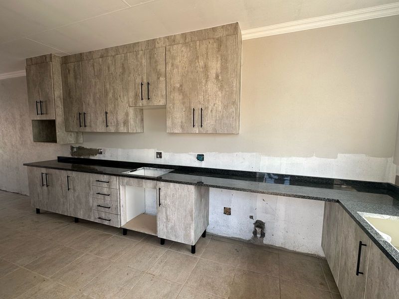 An unfinished kitchen featuring modern wood-look cabinetry and granite countertops, requiring backsplash installation and final wall finishing to complete the space.