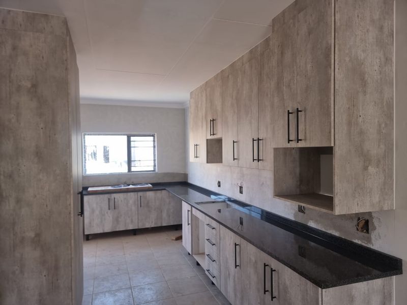 A modern, empty kitchen featuring wood-look cabinetry, dark granite countertops, and tiled flooring, awaiting final electrical finishing touches.