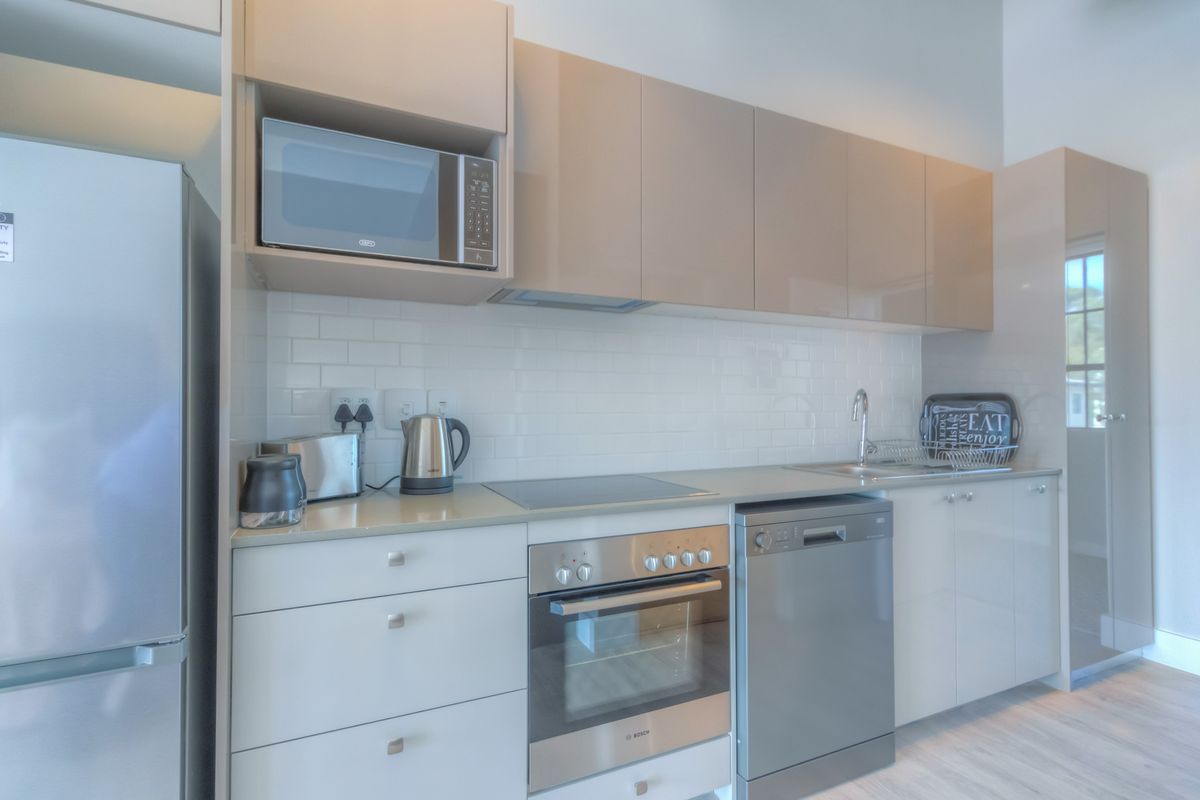 Modern kitchen featuring sleek high-gloss cabinetry, subway tile backsplash, integrated microwave, built-in oven, electric hob, and stainless steel dishwasher.