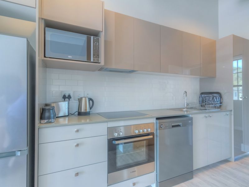 Modern kitchen featuring sleek high-gloss cabinetry, subway tile backsplash, integrated microwave, built-in oven, electric hob, and stainless steel dishwasher.