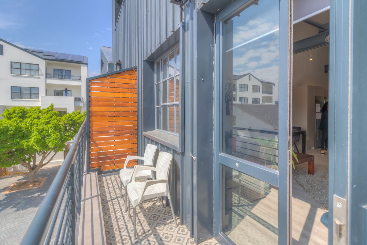 A modern balcony featuring patterned floor tiles, a timber privacy screen, and metal cladding, providing a seamless transition to the interior living space.