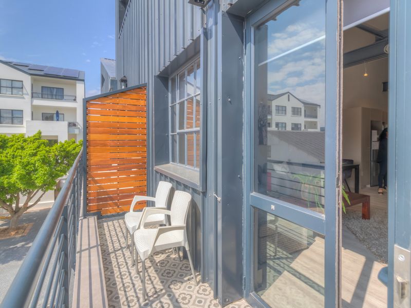 A modern balcony featuring patterned floor tiles, a timber privacy screen, and metal cladding, providing a seamless transition to the interior living space.