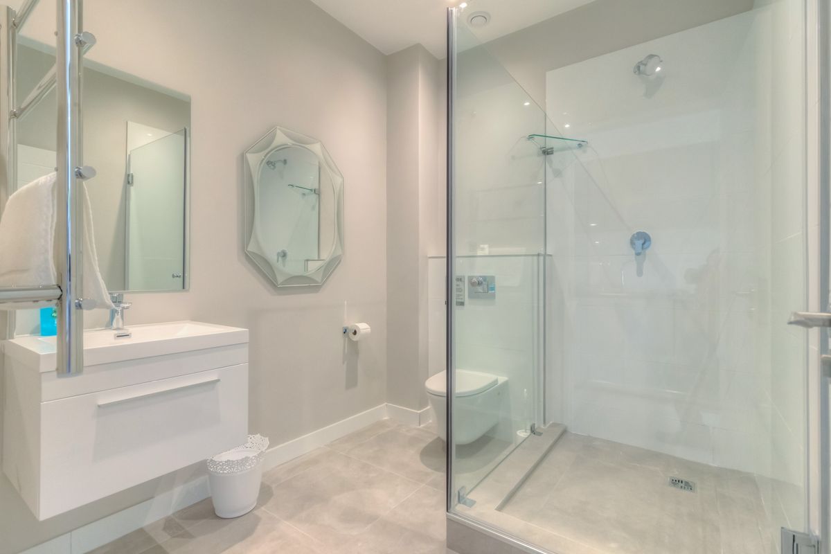 Modern bathroom featuring a wall-mounted vanity, wall-hung toilet, and a spacious glass-enclosed shower with contemporary tiled finishes.