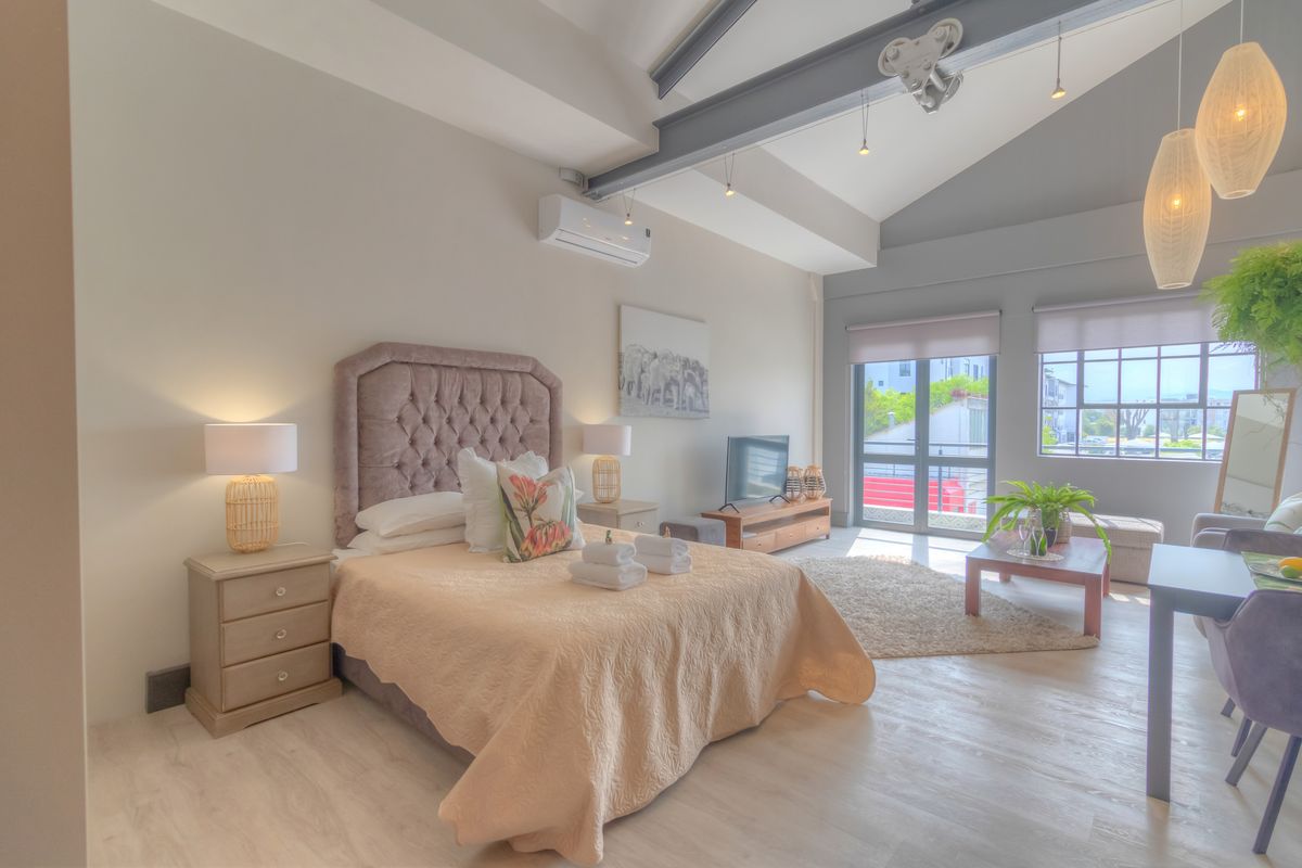 Spacious bedroom featuring vaulted ceilings with exposed steel beams, light laminate flooring, and a wall-mounted air conditioning unit.