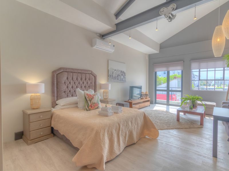 Spacious bedroom featuring vaulted ceilings with exposed steel beams, light laminate flooring, and a wall-mounted air conditioning unit.
