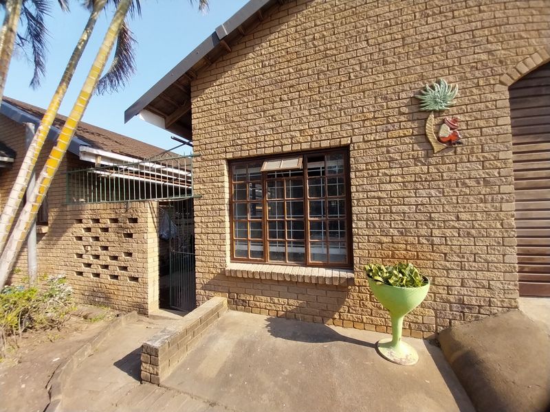 Front exterior view of a face brick cottage featuring steel-framed windows with security bars and a concrete entrance pathway.