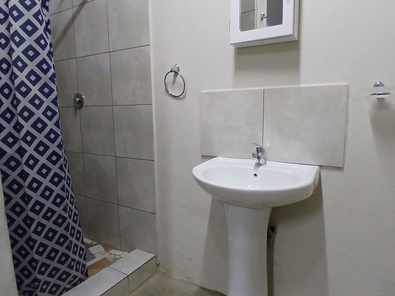 A functional bathroom featuring a pedestal basin, medicine cabinet, and a tiled shower enclosure with a shower curtain.