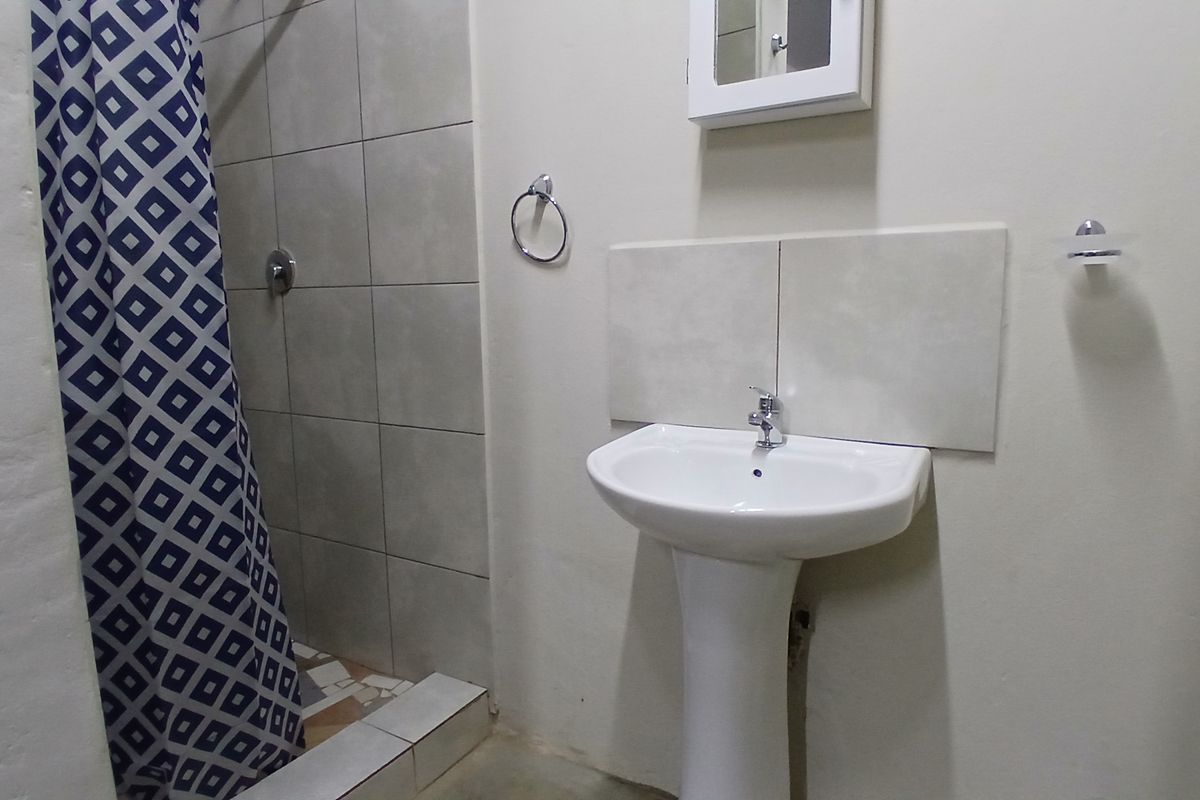 A functional bathroom featuring a pedestal basin, medicine cabinet, and a tiled shower enclosure with a shower curtain.